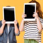 Photo of two children covering their faces with tablets