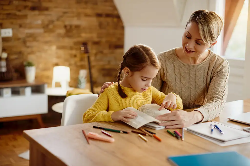 Image of a young girl reading a book with the help of her mother
